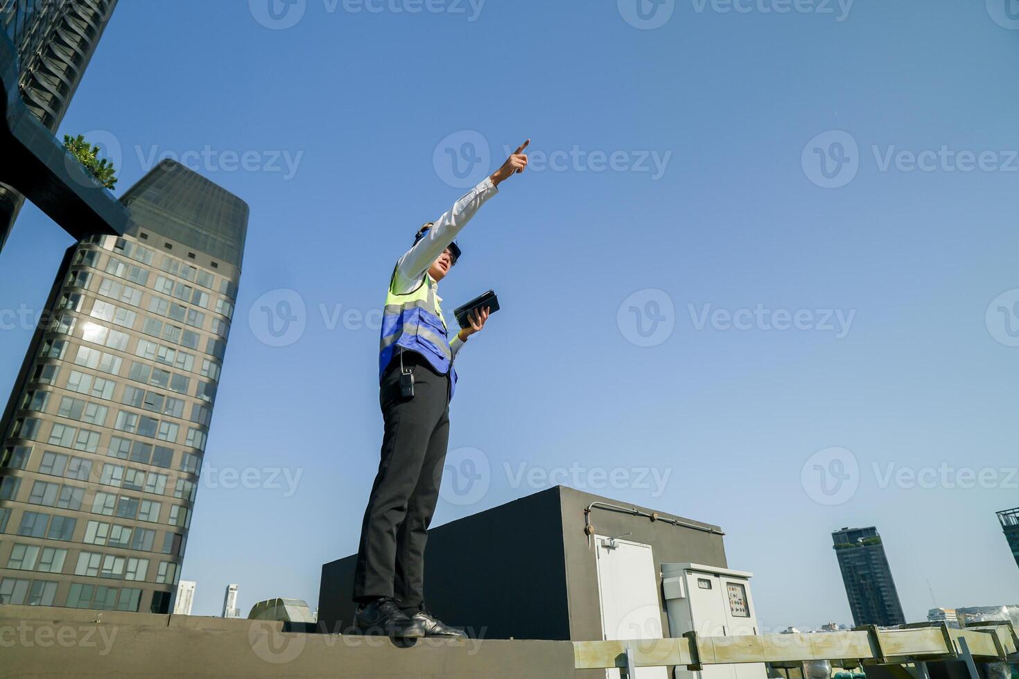 Skilled engineer operating tablet to manage HVAC machinery on top of building, urban architecture in distance. photo