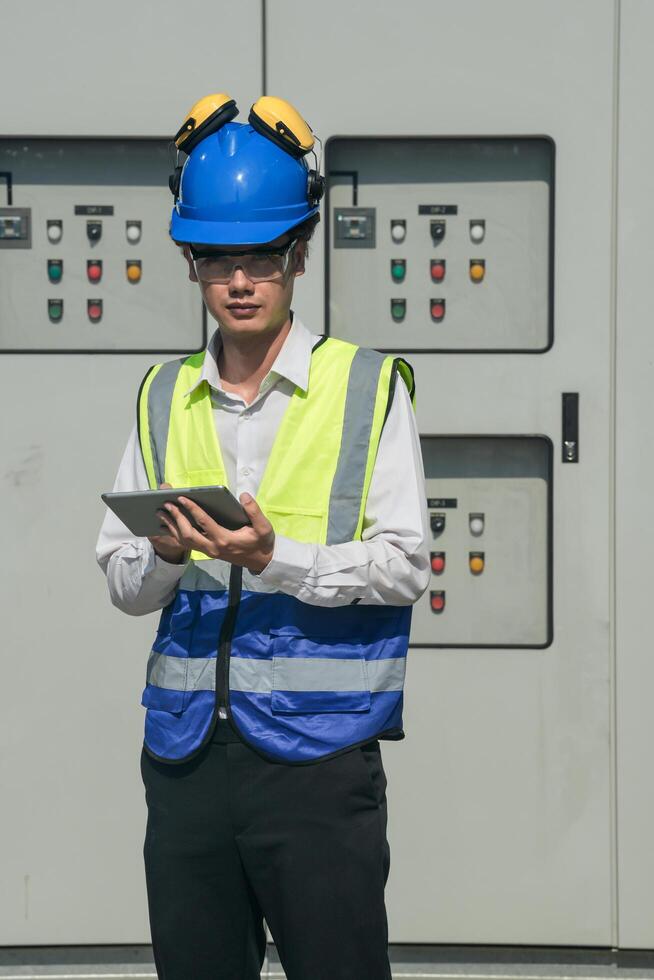 Focused young technician in safety gear inspects and controls industrial electrical equipment on a modern technical. photo