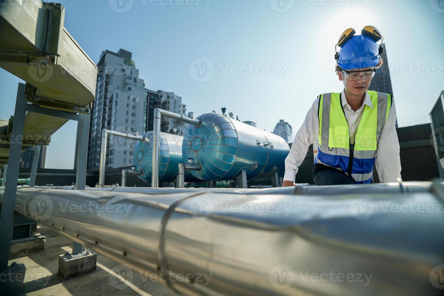 Urban rooftop scene showing a young engineer with a radio, inspecting and adjusting equipment in a sunny city environment. Safety and precision at work. photo