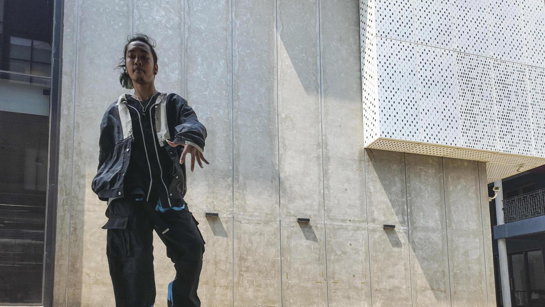 ASian man is dancing in hip hop style at outdoor space. Professional solo dancer is performing in public area. photo
