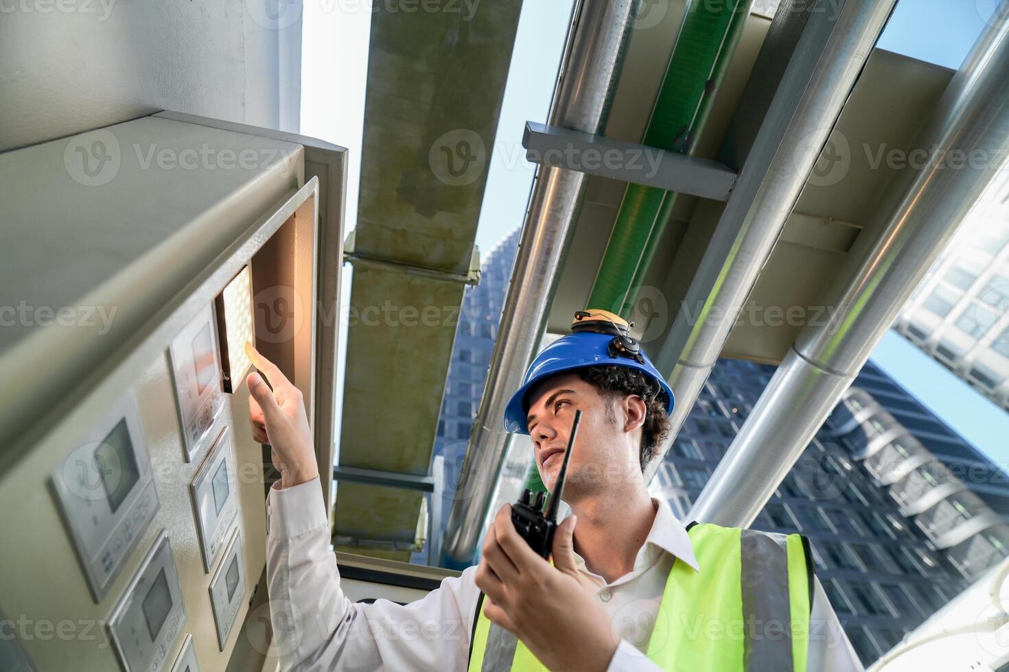 Industrial engineer adjusting pipeline valve with radio communication on construction site. Engineer on urban construction site using radio to coordinate with team on a sunny industrial rooftop. photo