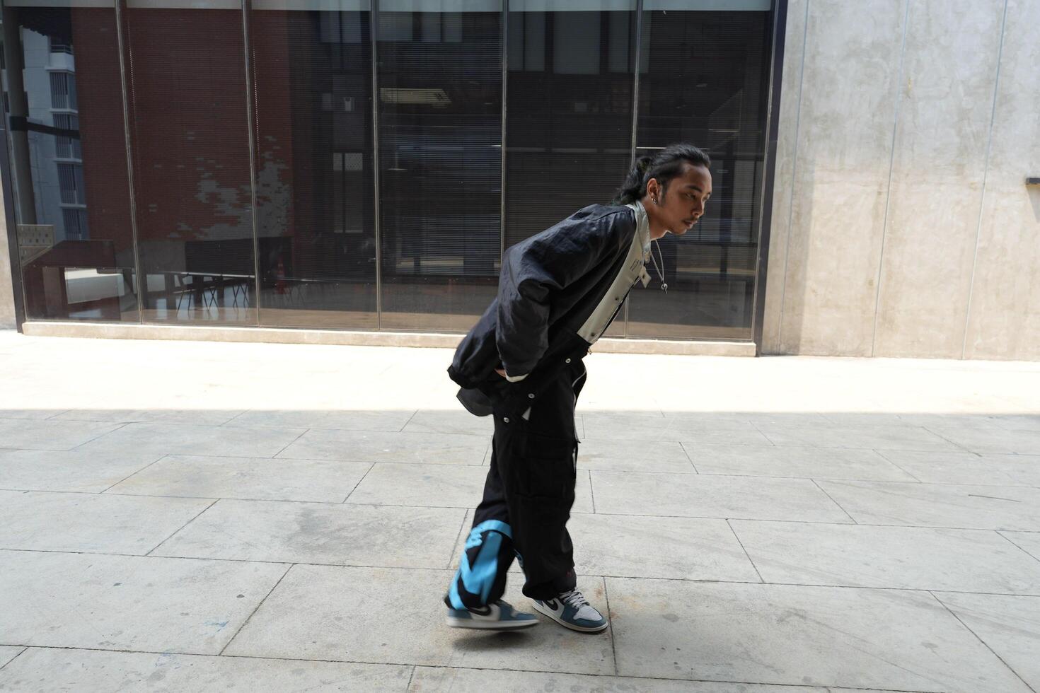 ASian man is dancing in hip hop style at outdoor space. Professional solo dancer is performing in public area. photo