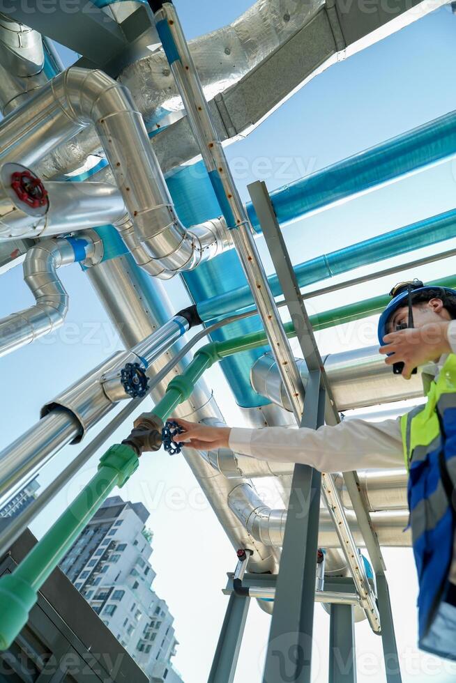 Industrial engineer adjusting pipeline valve with radio communication on construction site. Engineer on urban construction site using radio to coordinate with team on a sunny industrial rooftop. photo