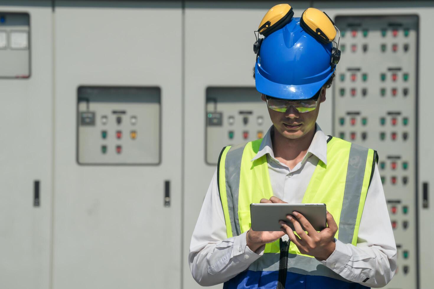 Focused young technician in safety gear inspects and controls industrial electrical equipment on a modern technical. photo