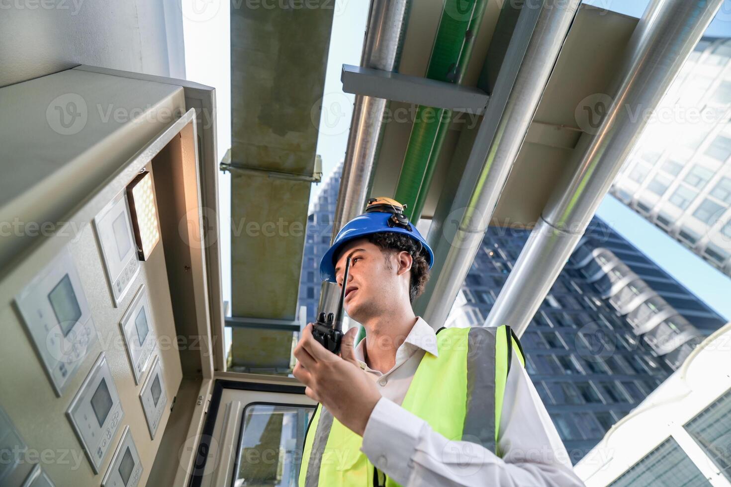 Industrial engineer adjusting pipeline valve with radio communication on construction site. Engineer on urban construction site using radio to coordinate with team on a sunny industrial rooftop. photo