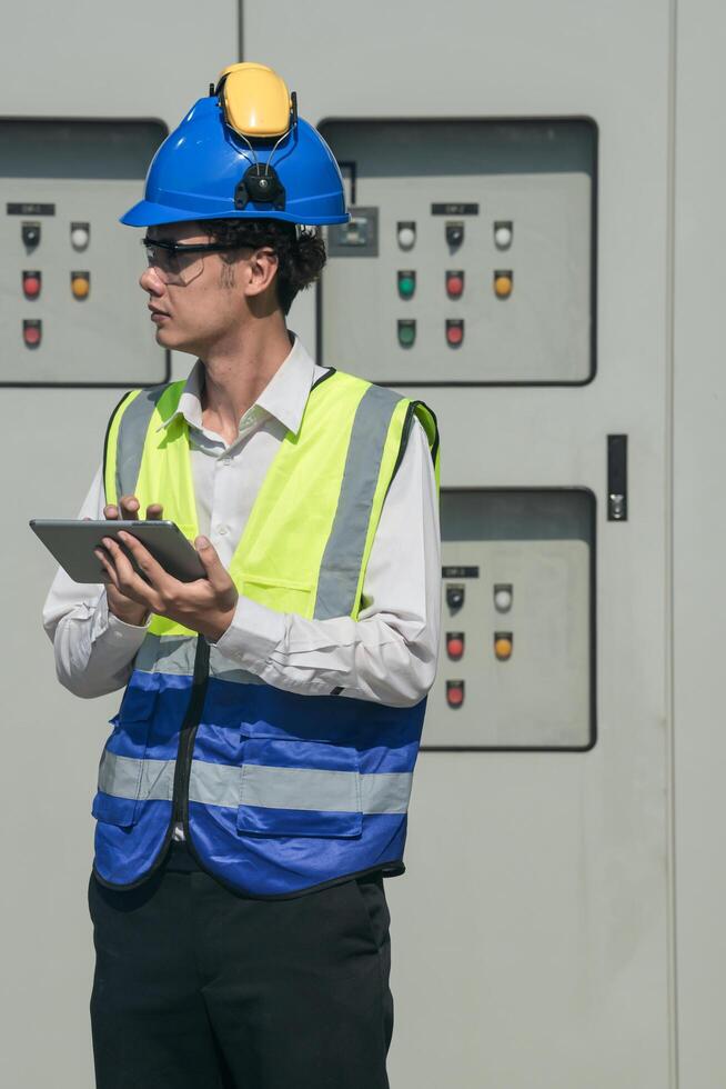 Focused young technician in safety gear inspects and controls industrial electrical equipment on a modern technical. photo