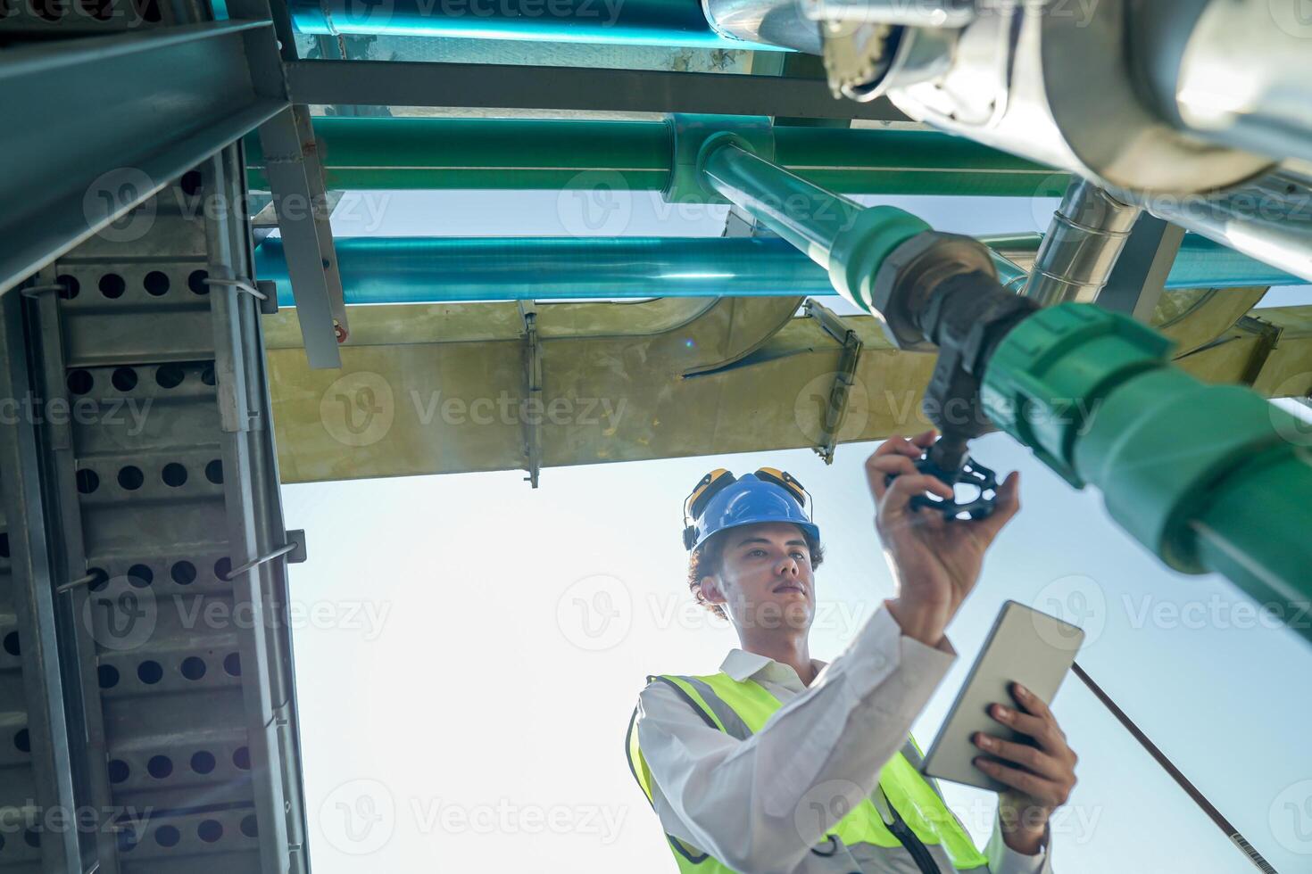 Male engineer monitoring machinery on a rooftop with city skyline in the background, wearing safety gear photo