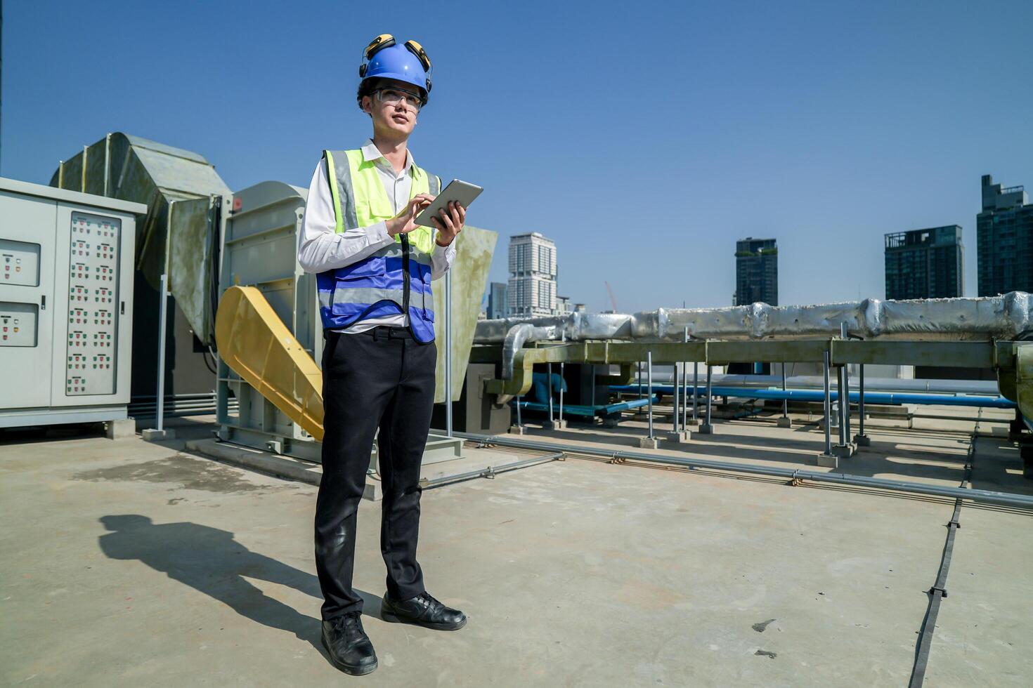 Skilled engineer operating tablet to manage HVAC machinery on top of building, urban architecture in distance. photo
