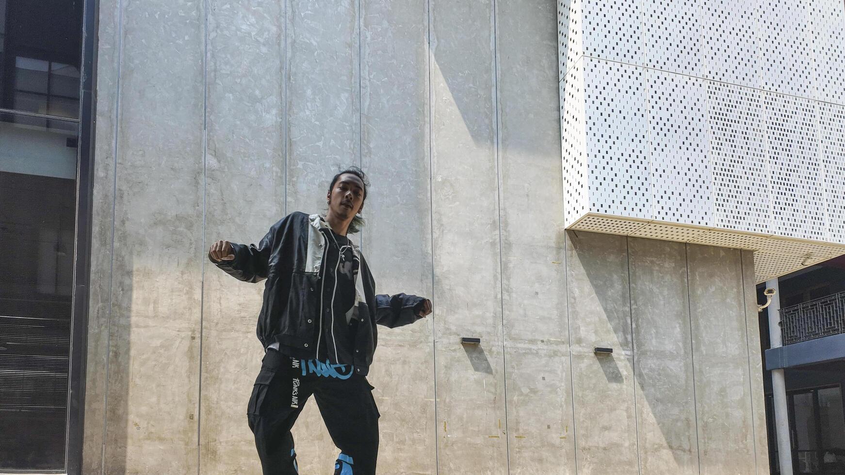 ASian man is dancing in hip hop style at outdoor space. Professional solo dancer is performing in public area. photo
