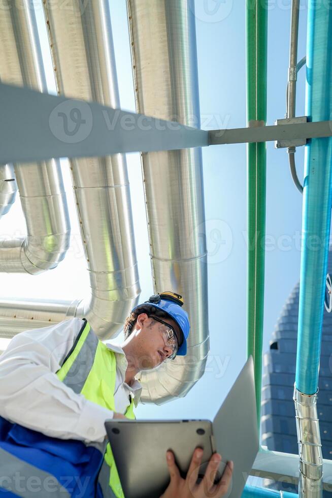 Industrial engineer adjusting pipeline valve with radio communication on construction site. Engineer on urban construction site using radio to coordinate with team on a sunny industrial rooftop. photo