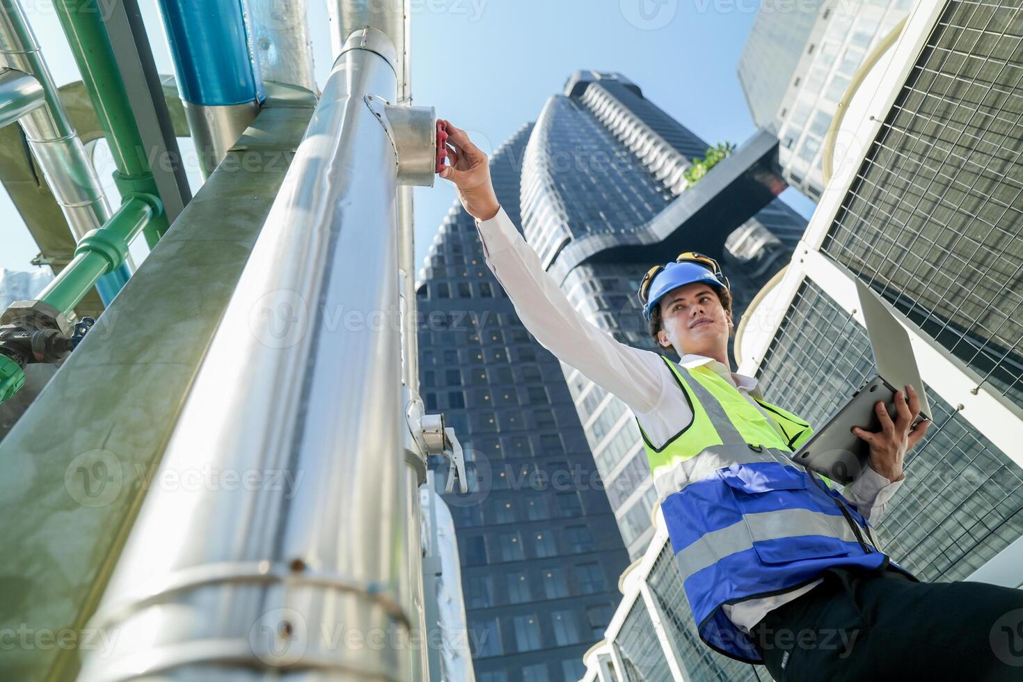 Industrial engineer adjusting pipeline valve with radio communication on construction site. Engineer on urban construction site using radio to coordinate with team on a sunny industrial rooftop. photo