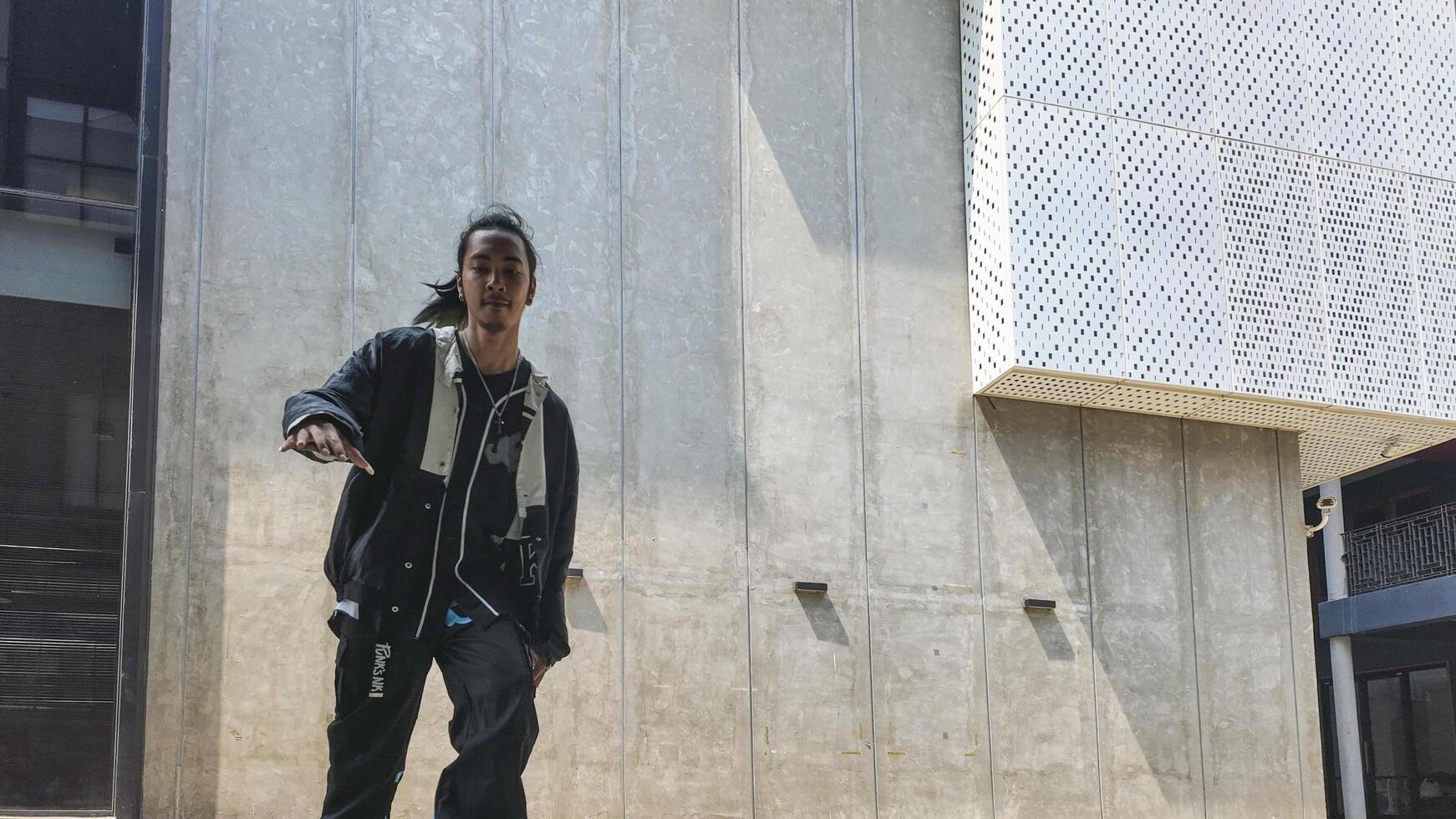 ASian man is dancing in hip hop style at outdoor space. Professional solo dancer is performing in public area. photo