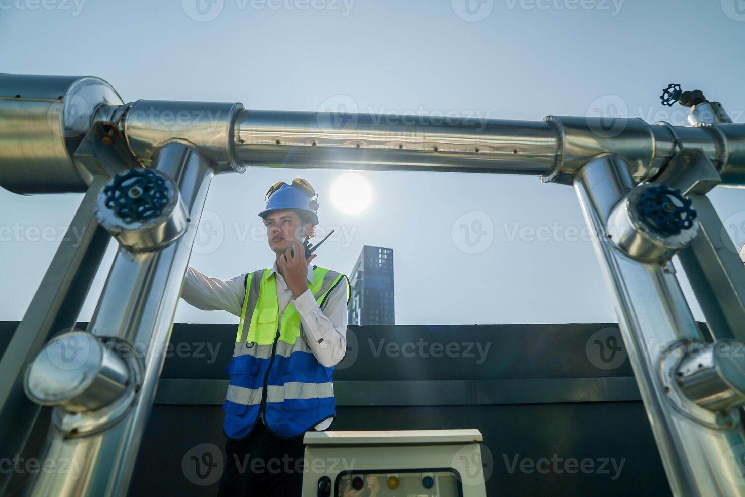 Engineer in safety gear conducts inspection on large industrial water tanks on a building rooftop. Professional engineer meticulously checks connectivity and status of piping on an urban rooftop. photo