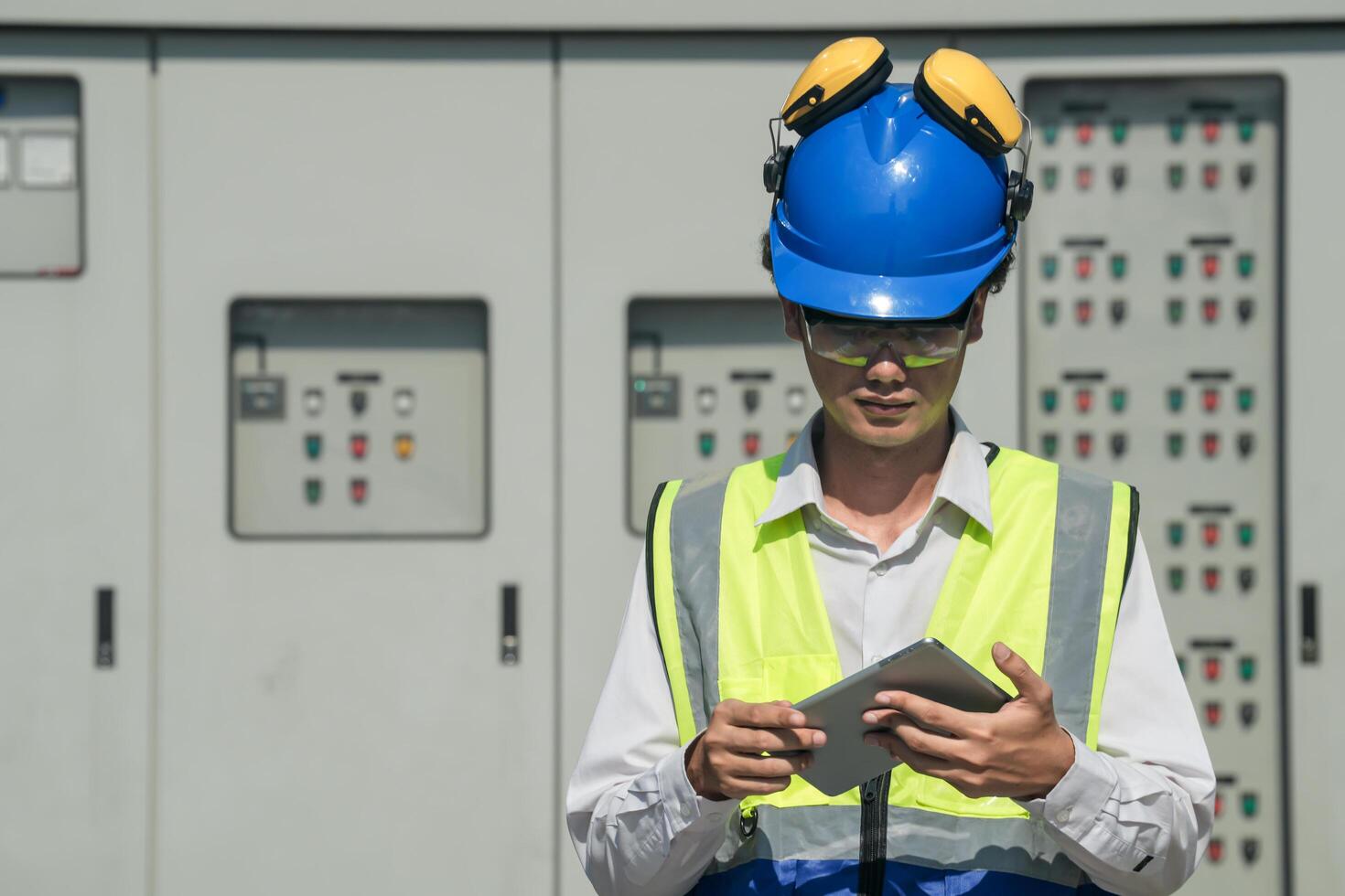 Focused young technician in safety gear inspects and controls industrial electrical equipment on a modern technical. photo