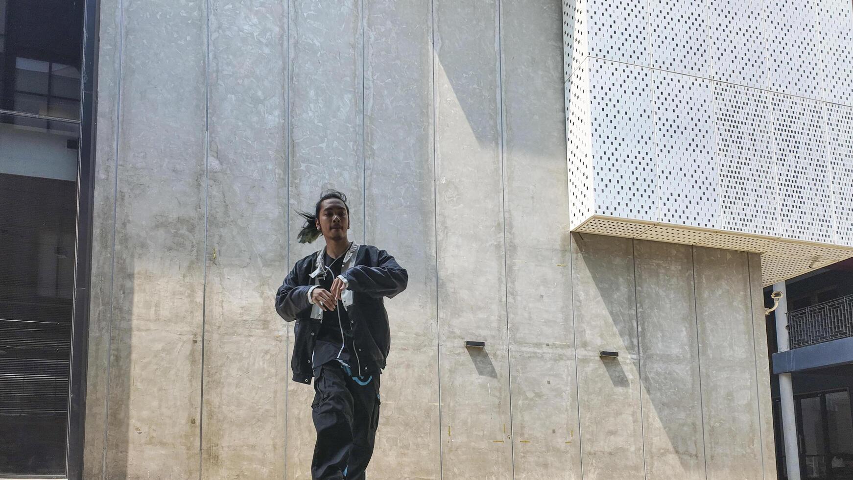 ASian man is dancing in hip hop style at outdoor space. Professional solo dancer is performing in public area. photo