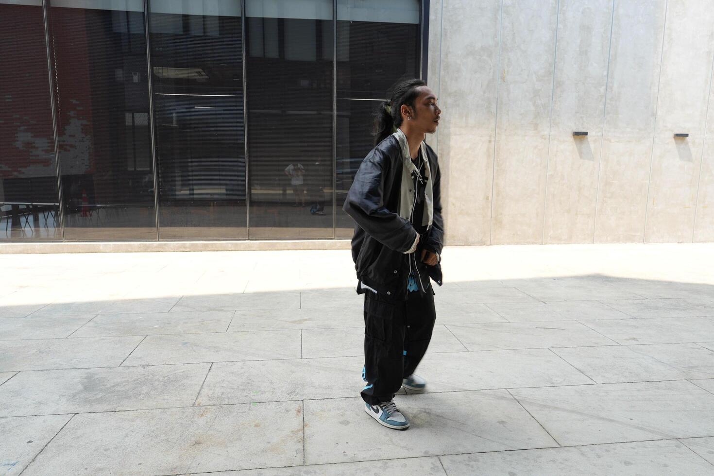 ASian man is dancing in hip hop style at outdoor space. Professional solo dancer is performing in public area. photo