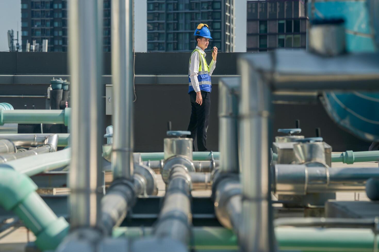 A professional engineer communicates via walkie-talkie on a building's rooftop, surrounded by piping and ductwork. photo