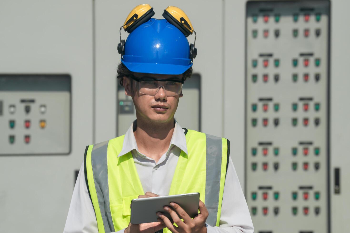 Focused young technician in safety gear inspects and controls industrial electrical equipment on a modern technical. photo
