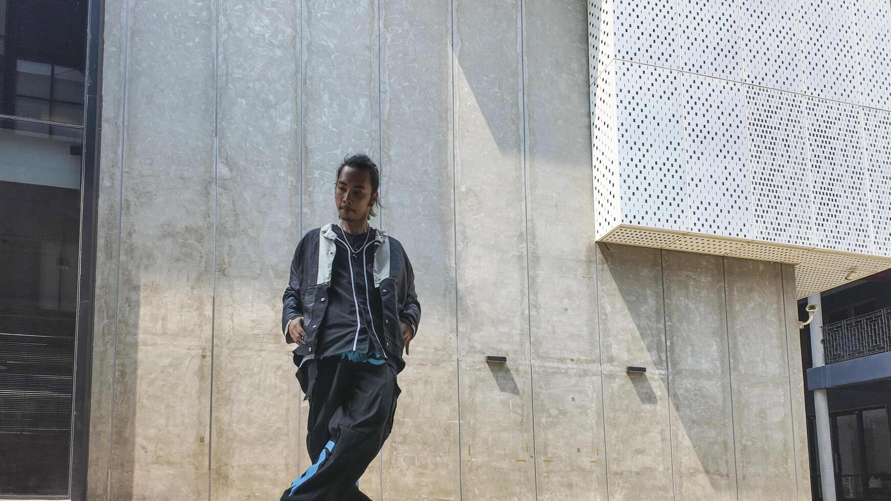 ASian man is dancing in hip hop style at outdoor space. Professional solo dancer is performing in public area. photo