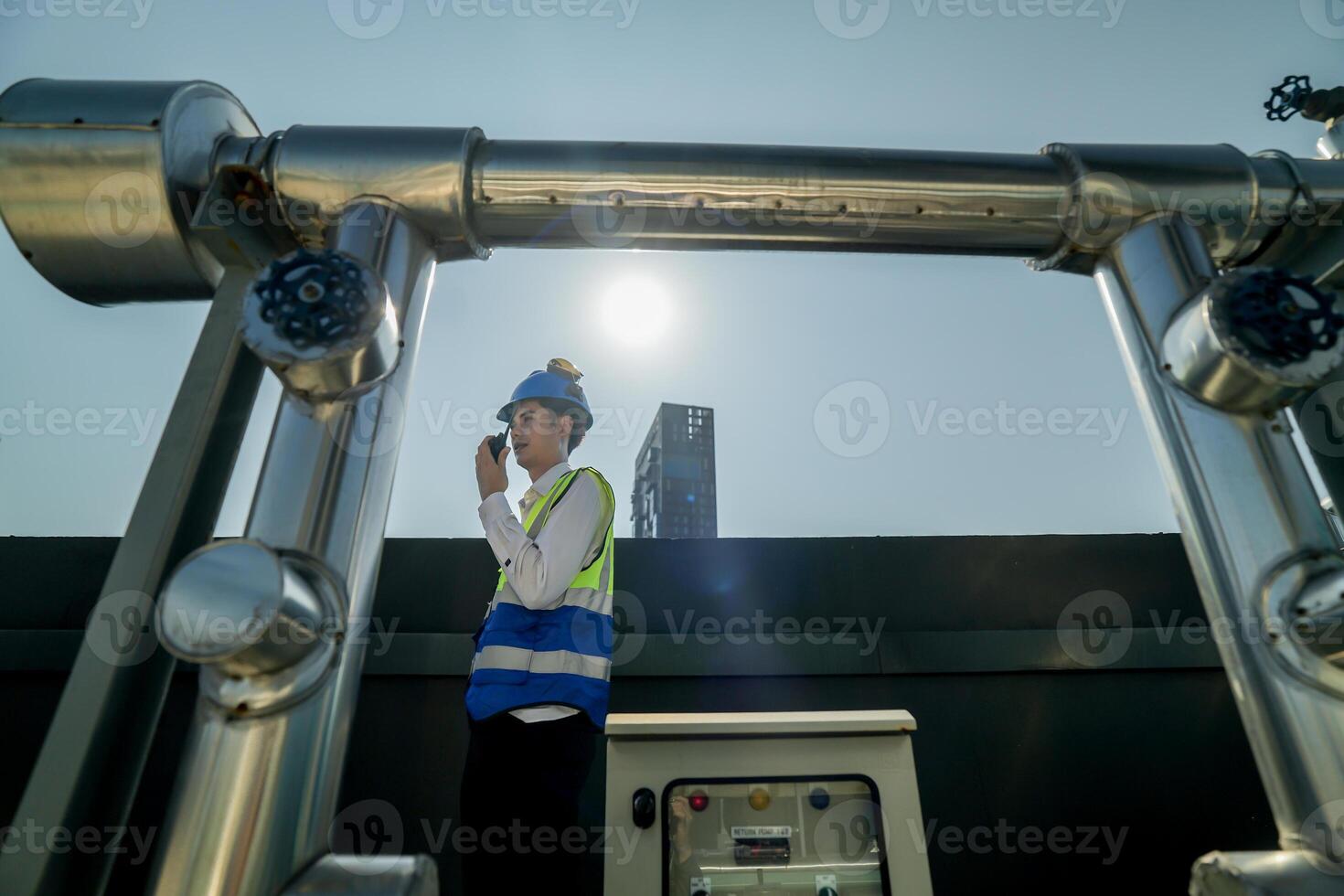 Engineer in safety gear conducts inspection on large industrial water tanks on a building rooftop. Professional engineer meticulously checks connectivity and status of piping on an urban rooftop. photo