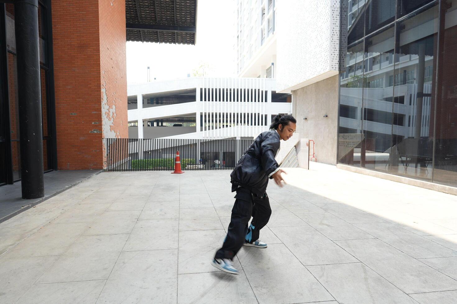ASian man is dancing in hip hop style at outdoor space. Professional solo dancer is performing in public area. photo