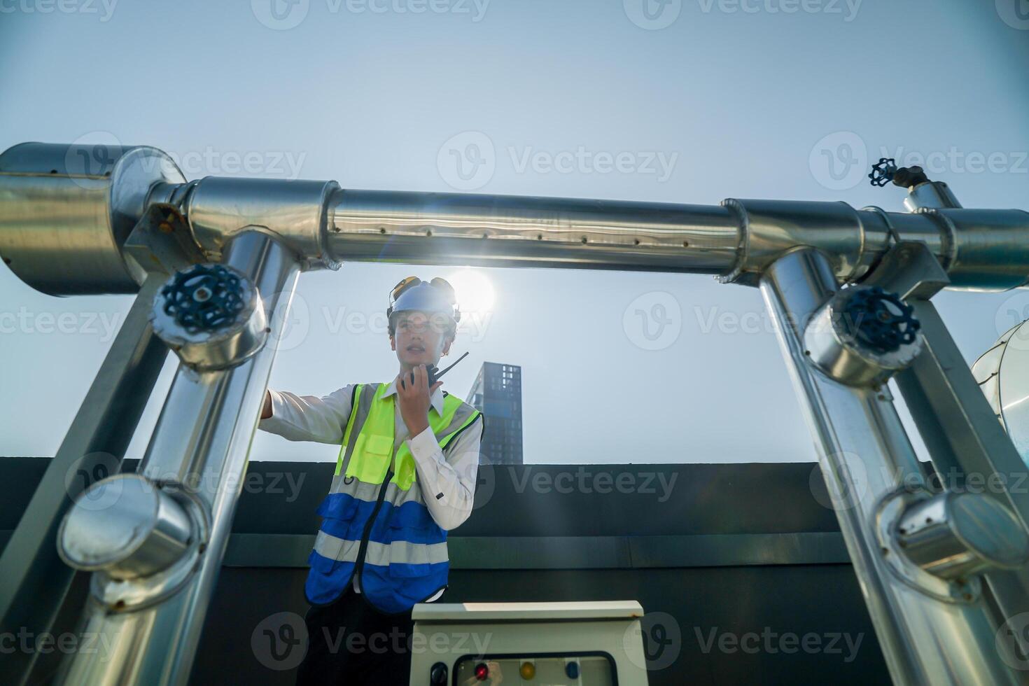 Engineer in safety gear conducts inspection on large industrial water tanks on a building rooftop. Professional engineer meticulously checks connectivity and status of piping on an urban rooftop. photo