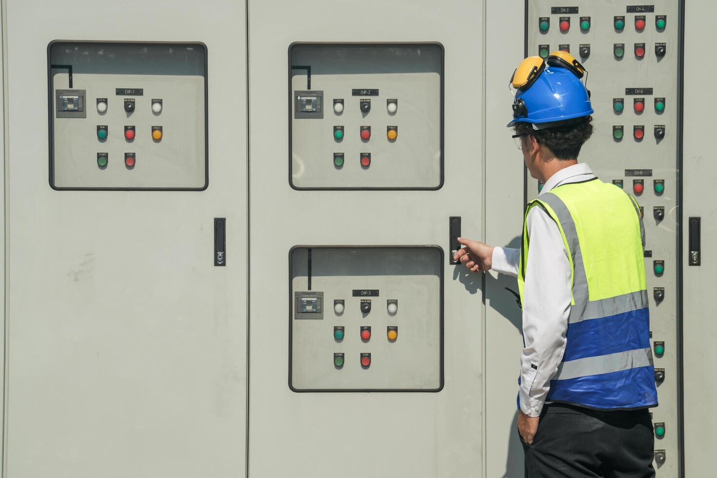 Focused young technician in safety gear inspects and controls industrial electrical equipment on a modern technical. photo