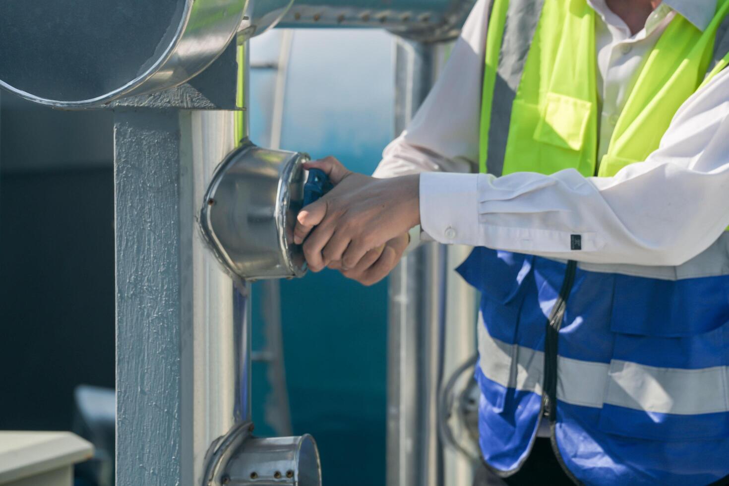 Focused engineer tightening valve with wrench at industrial plant, daylight setting. Technician in safety vest using wrench on industrial piping, clear day backdrop. photo