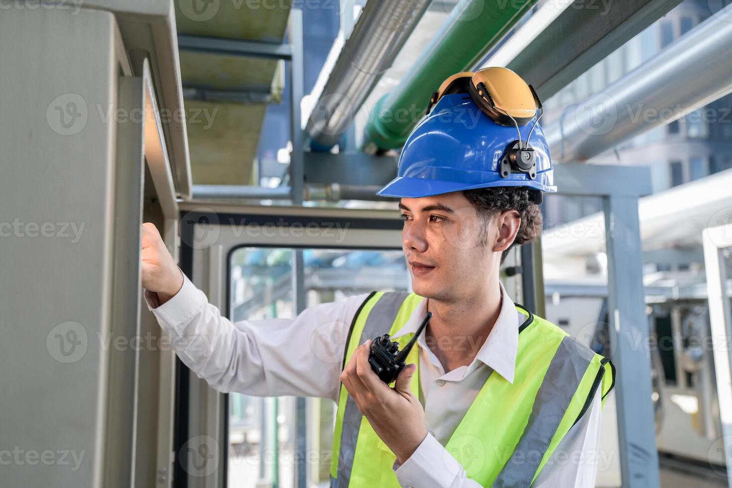 Industrial engineer adjusting pipeline valve with radio communication on construction site. Engineer on urban construction site using radio to coordinate with team on a sunny industrial rooftop. photo