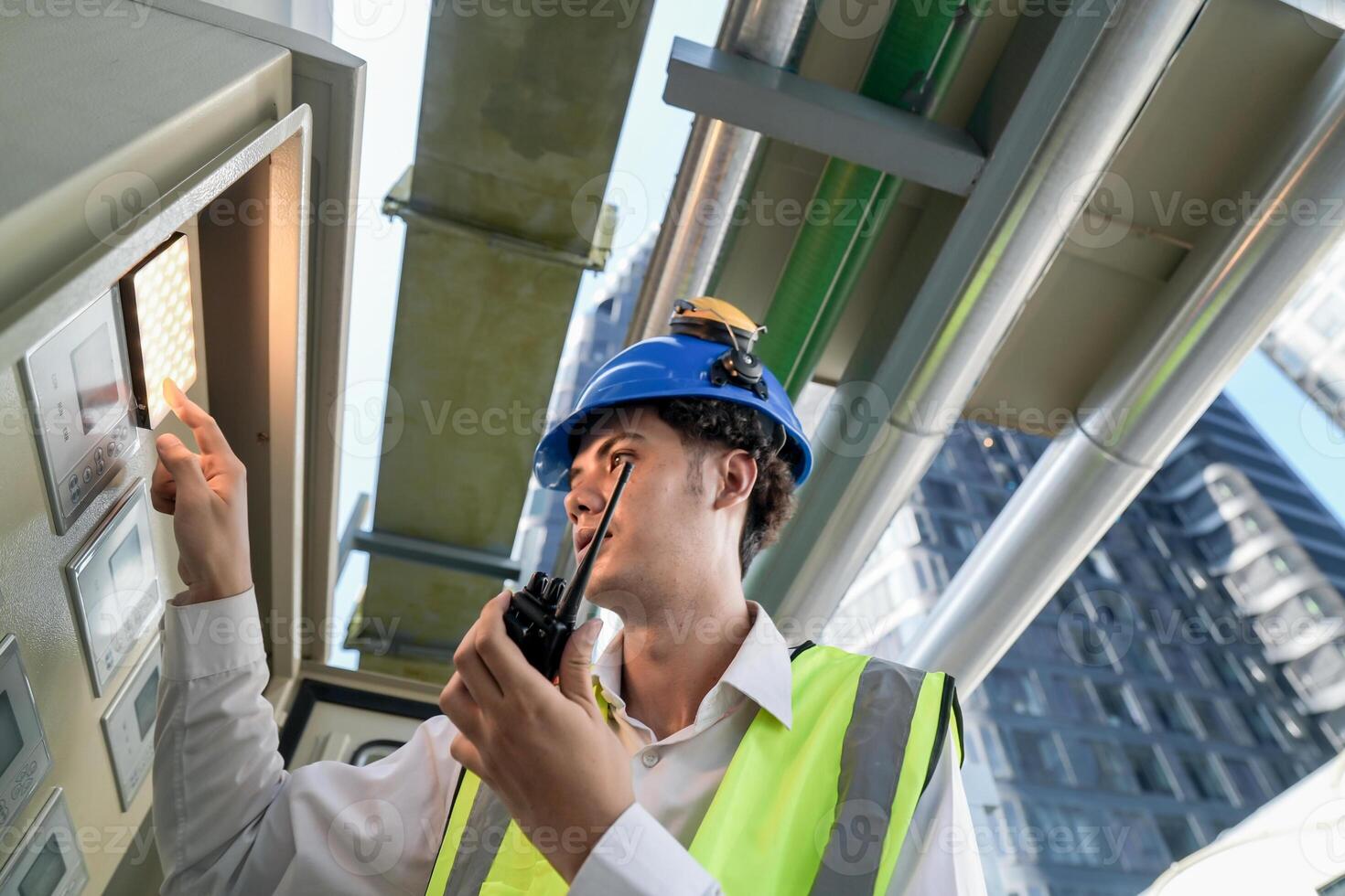 Industrial engineer adjusting pipeline valve with radio communication on construction site. Engineer on urban construction site using radio to coordinate with team on a sunny industrial rooftop. photo