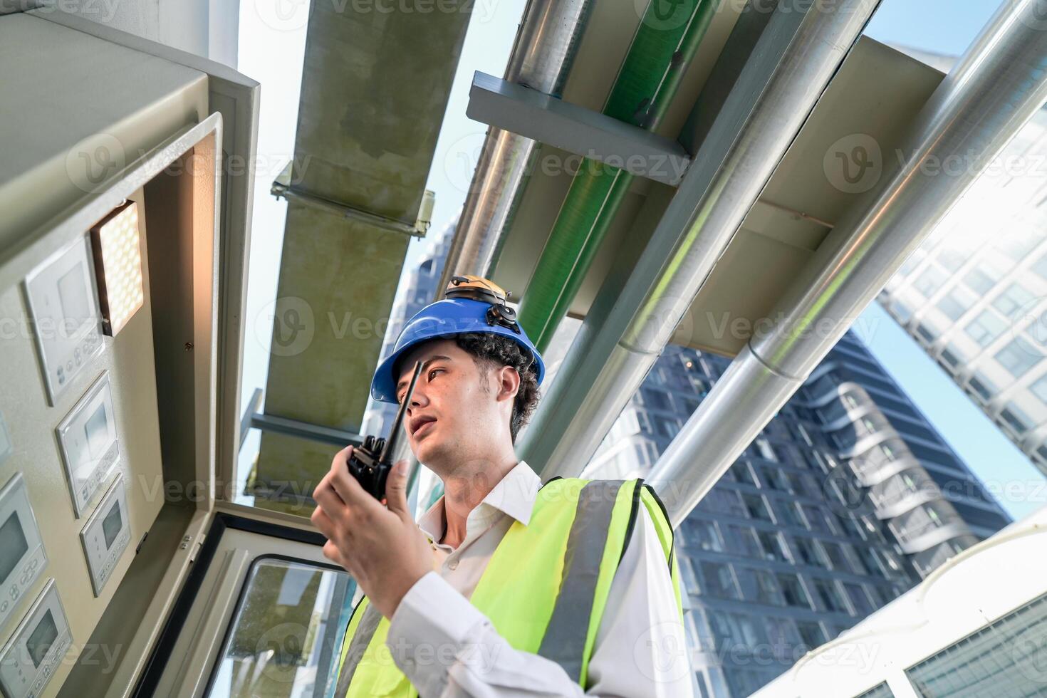Industrial engineer adjusting pipeline valve with radio communication on construction site. Engineer on urban construction site using radio to coordinate with team on a sunny industrial rooftop. photo