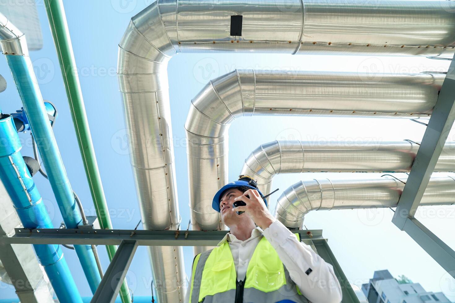 Industrial engineer adjusting pipeline valve with radio communication on construction site. Engineer on urban construction site using radio to coordinate with team on a sunny industrial rooftop. photo