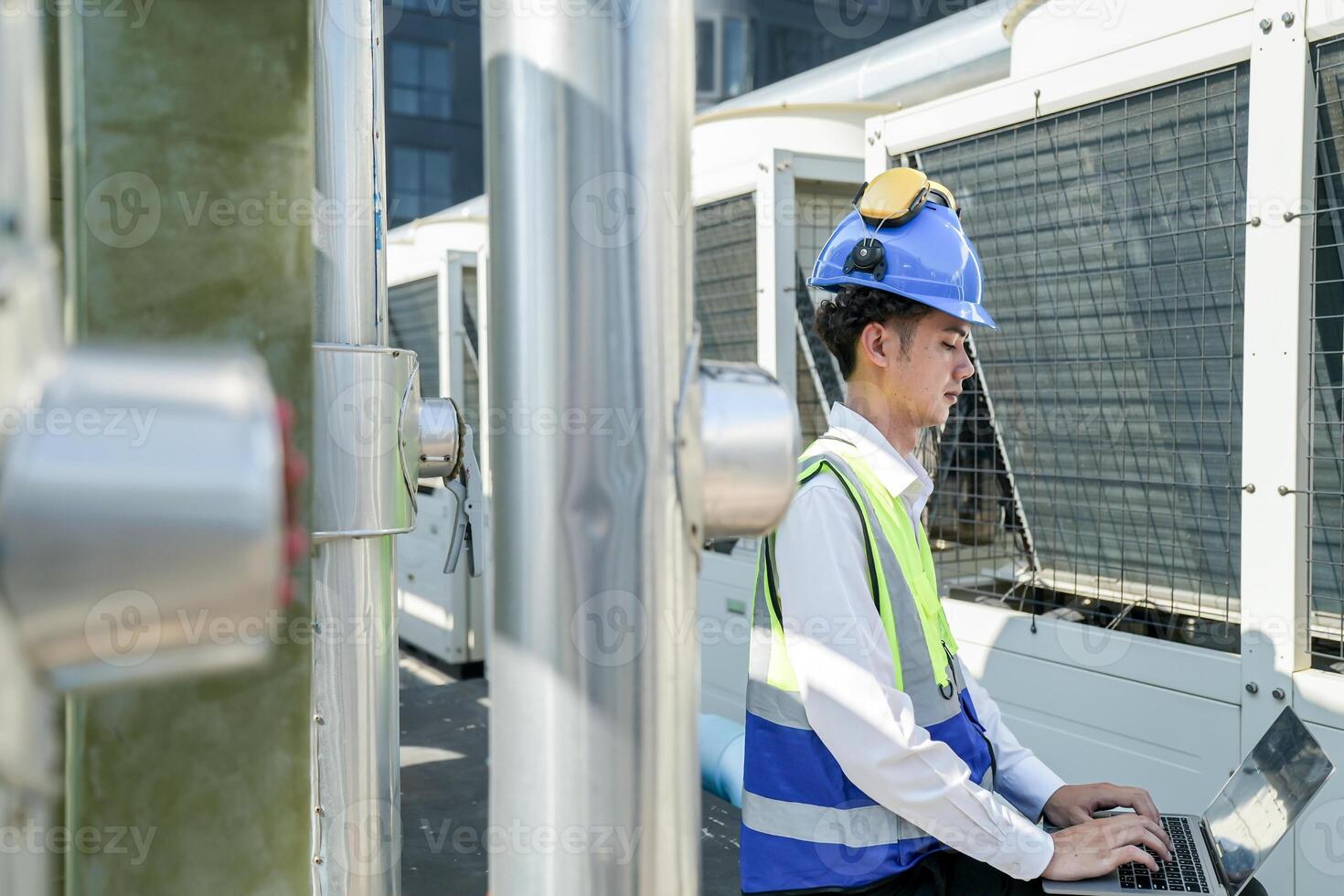 Industrial engineer adjusting pipeline valve with radio communication on construction site. Engineer on urban construction site using radio to coordinate with team on a sunny industrial rooftop. photo