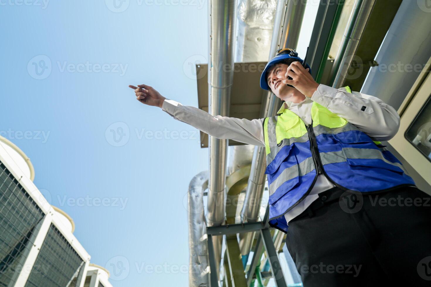 Industrial engineer adjusting pipeline valve with radio communication on construction site. Engineer on urban construction site using radio to coordinate with team on a sunny industrial rooftop. photo
