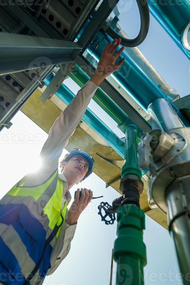 Industrial engineer adjusting pipeline valve with radio communication on construction site. Construction worker using walkie-talkie to coordinate machinery adjustments on a sunny day. photo