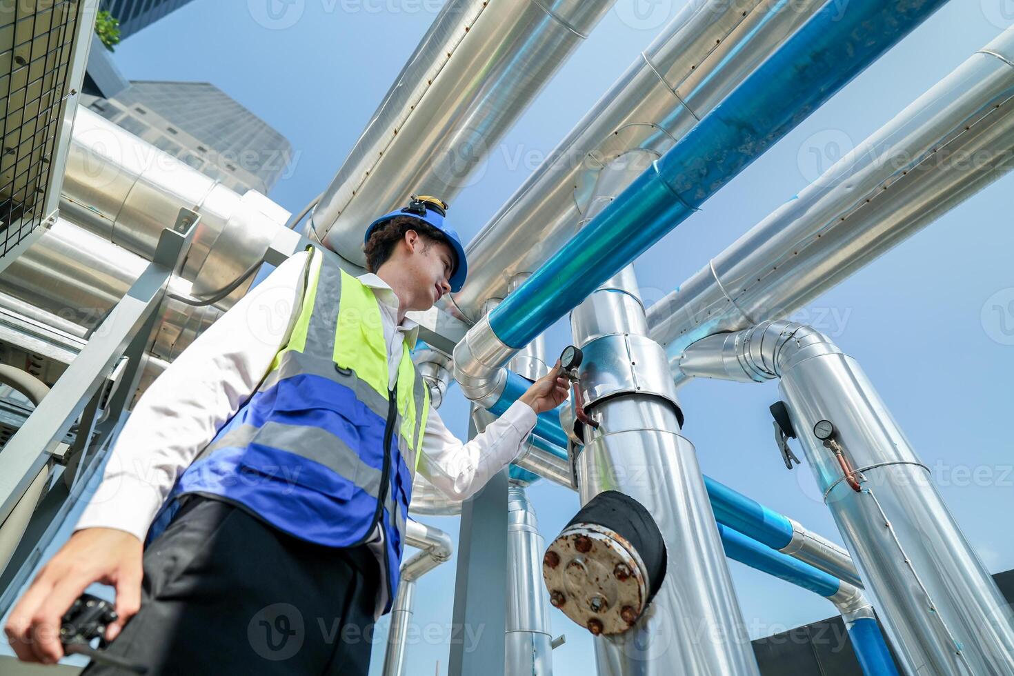 Industrial engineer adjusting pipeline valve with radio communication on construction site. Engineer on urban construction site using radio to coordinate with team on a sunny industrial rooftop. photo