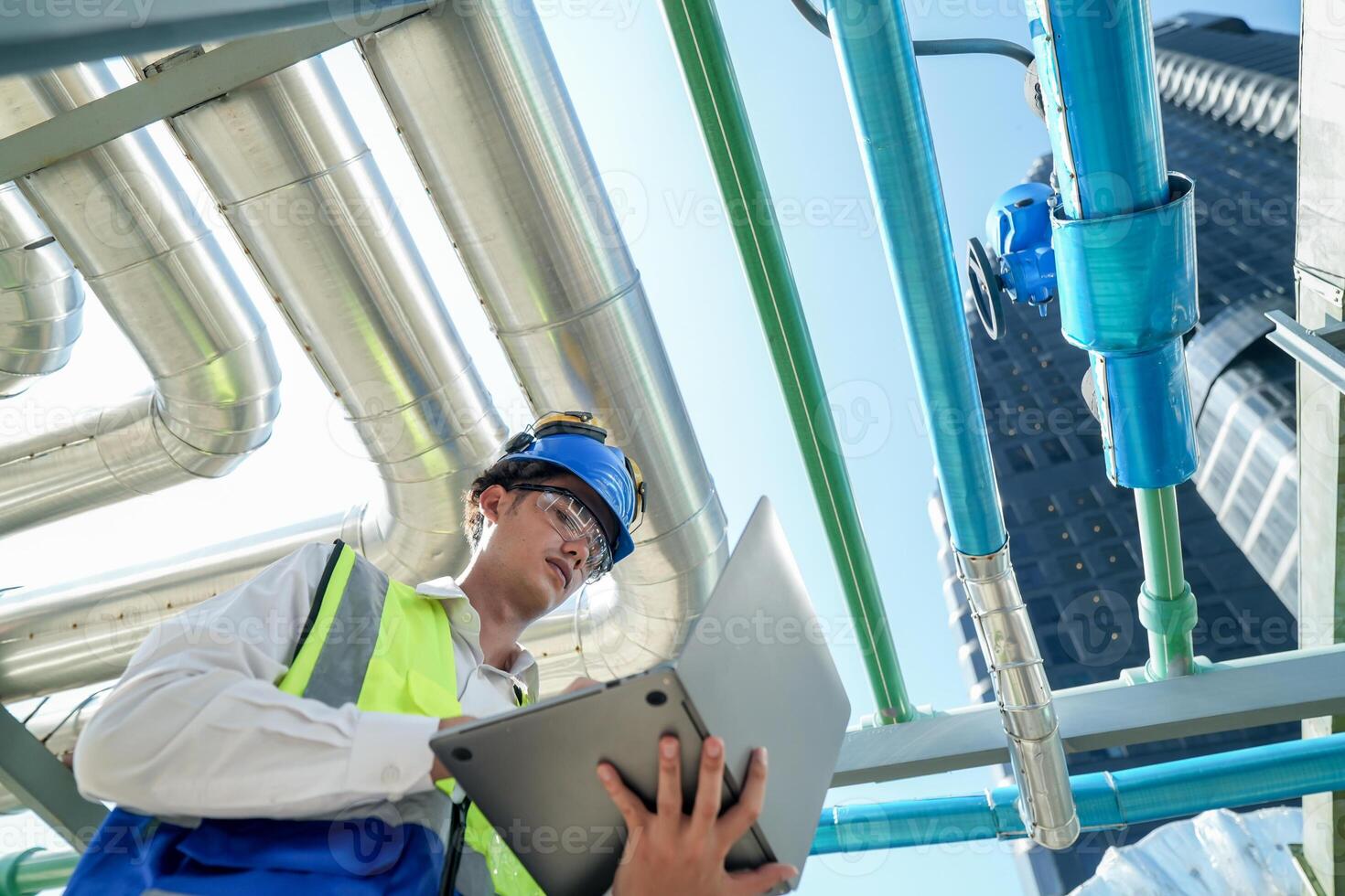 Industrial engineer adjusting pipeline valve with radio communication on construction site. Engineer on urban construction site using radio to coordinate with team on a sunny industrial rooftop. photo