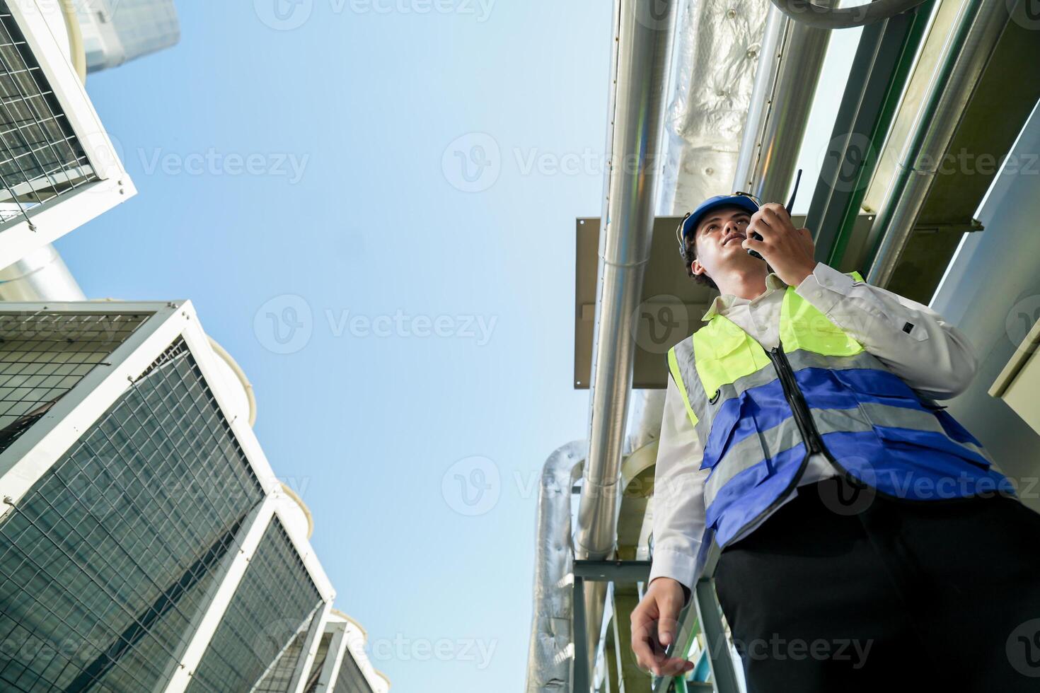 Industrial engineer adjusting pipeline valve with radio communication on construction site. Engineer on urban construction site using radio to coordinate with team on a sunny industrial rooftop. photo