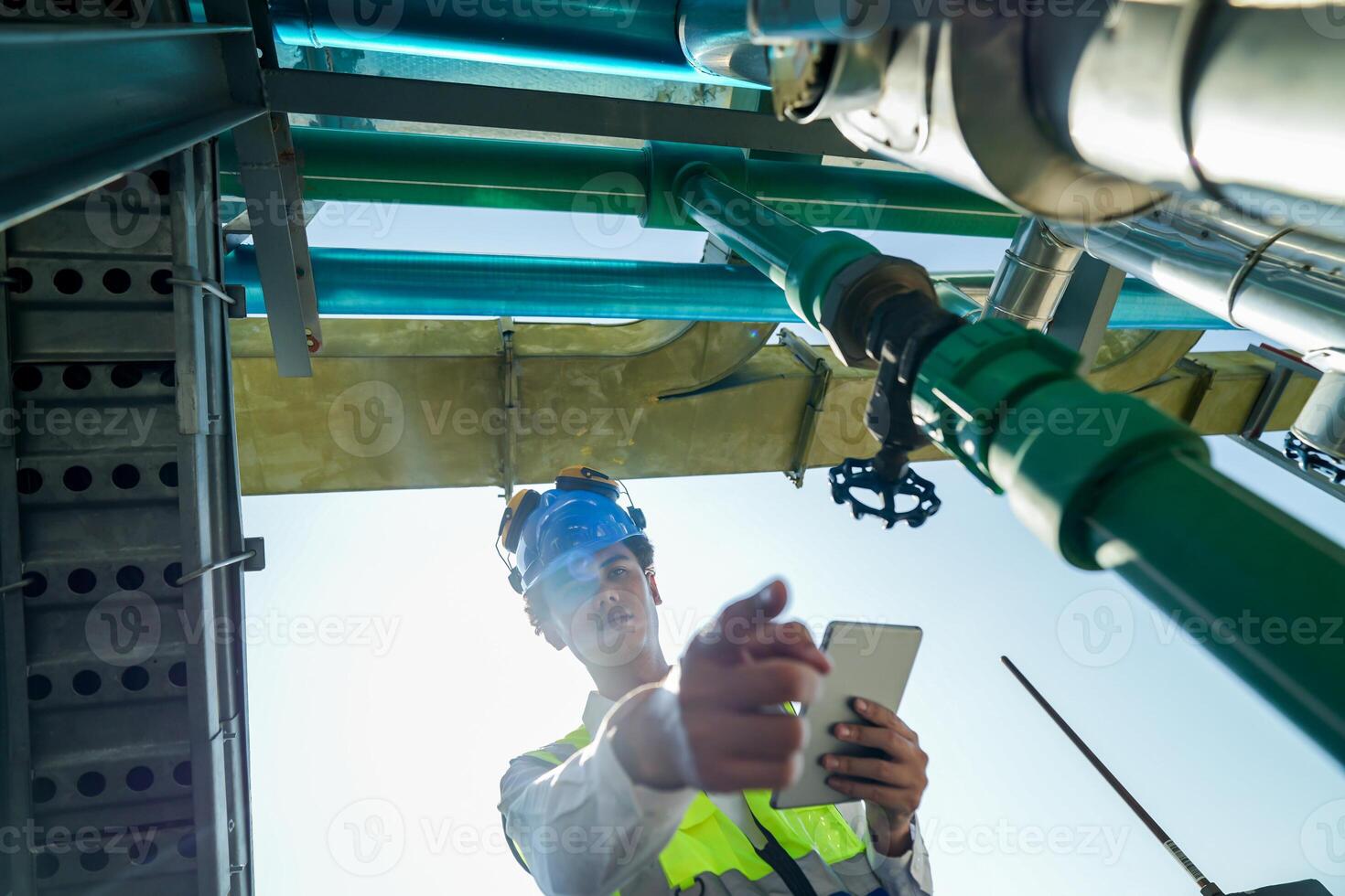 Industrial engineer adjusting pipeline valve with radio communication on construction site. Construction worker using walkie-talkie to coordinate machinery adjustments on a sunny day. photo