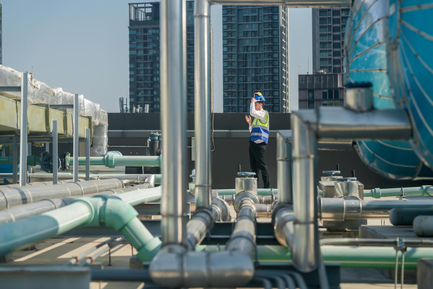 A professional engineer communicates via walkie-talkie on a building's rooftop, surrounded by piping and ductwork. photo