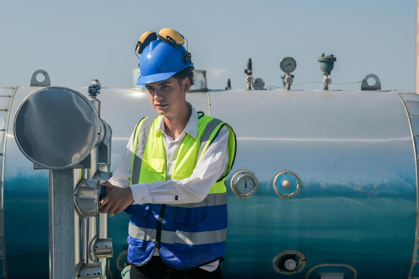 Industrial engineer with safety helmet operating a control panel outdoors. Cheerful engineer operates equipment on industrial site against a clear sky. photo