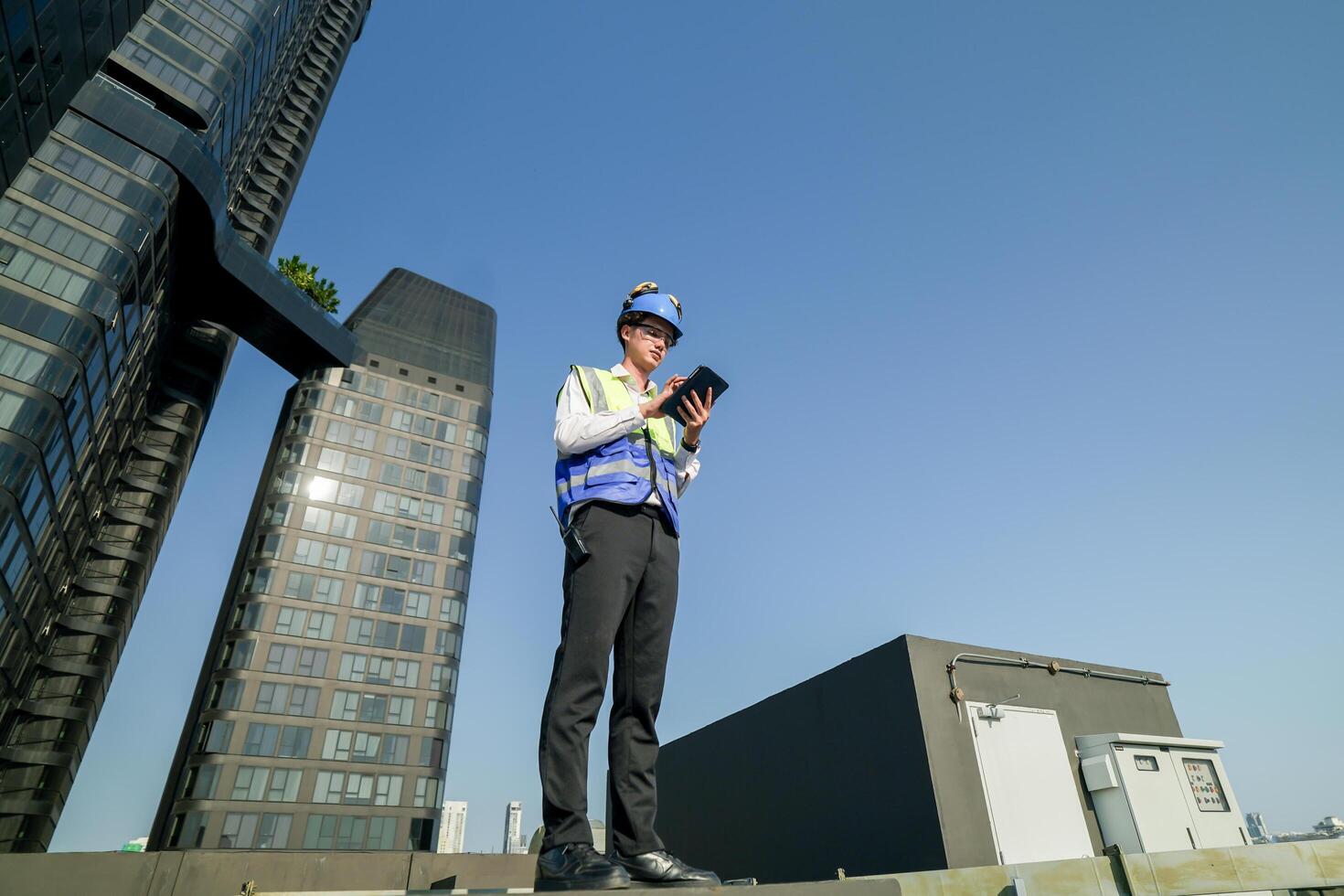 Skilled engineer operating tablet to manage HVAC machinery on top of building, urban architecture in distance. photo