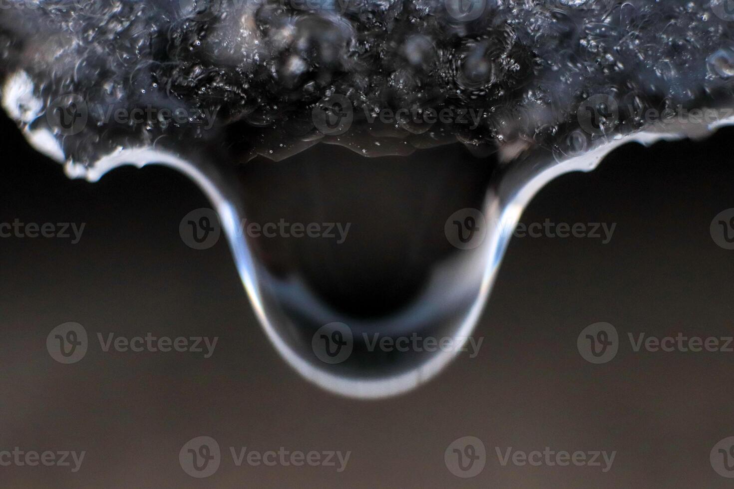 Handing down water drop from ice top. Cold clear rain drop with ice reflection inside. Macro closeup. photo