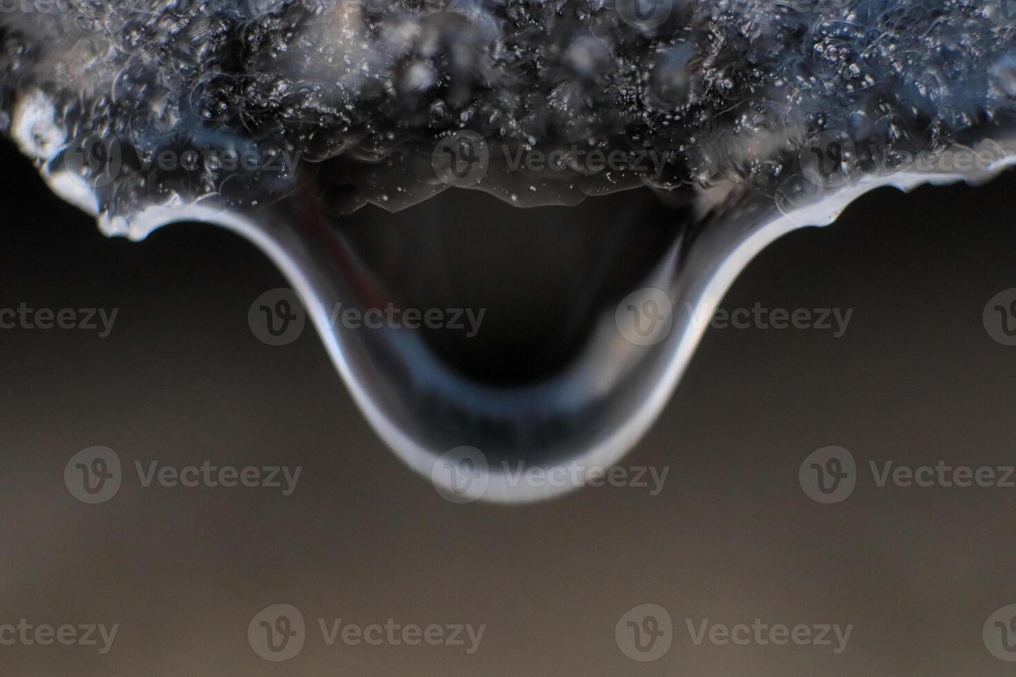 Cold clear rain drop with ice reflection inside. Handing down water drop from ice top. Macro closeup. photo