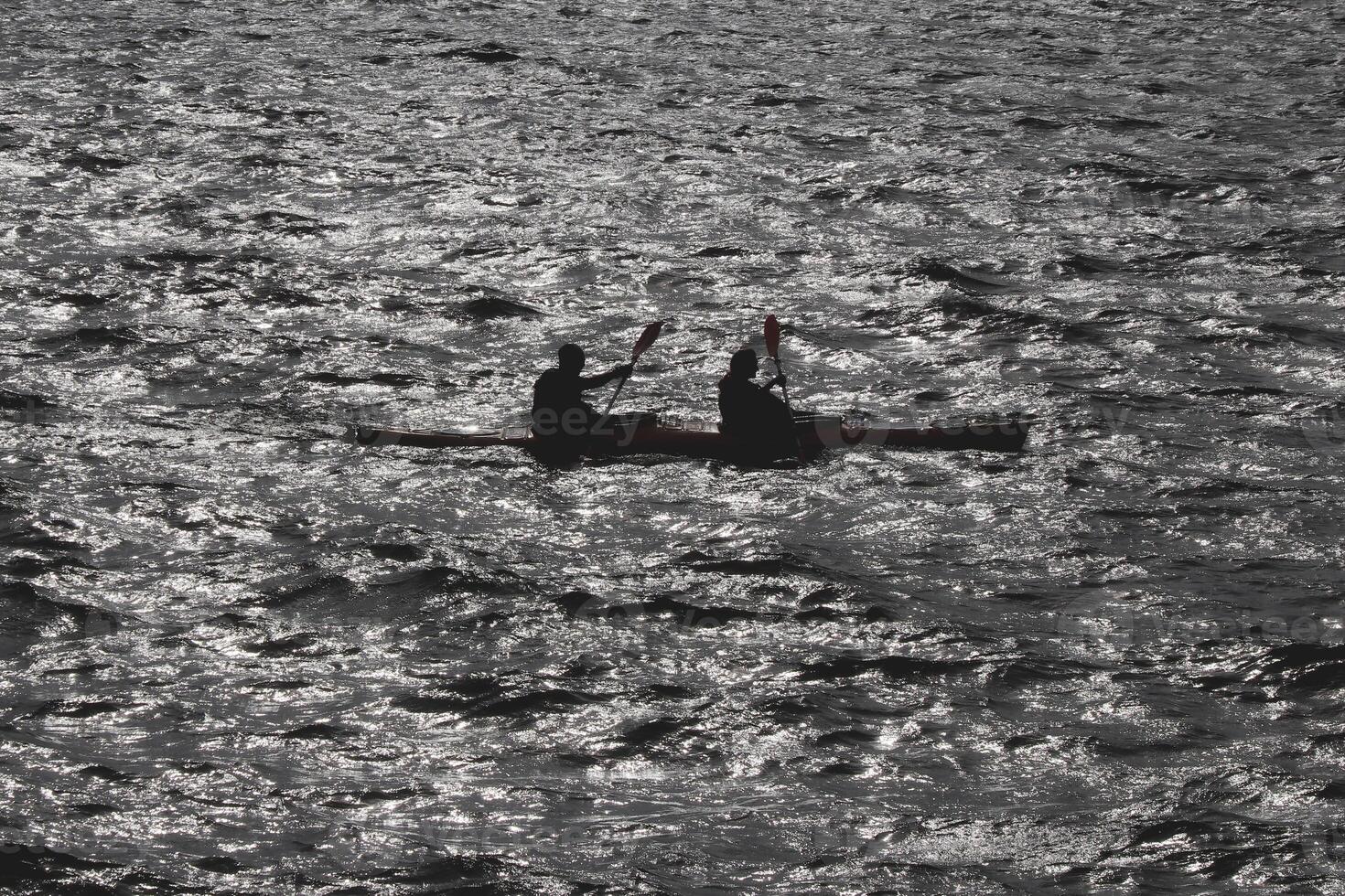 Two people go on a kayak along the bay in the reflection of sun glare on the water. photo