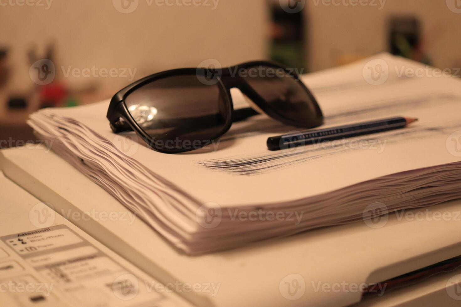 Sunglasses with pen lie on a stack of paper on the printer photo