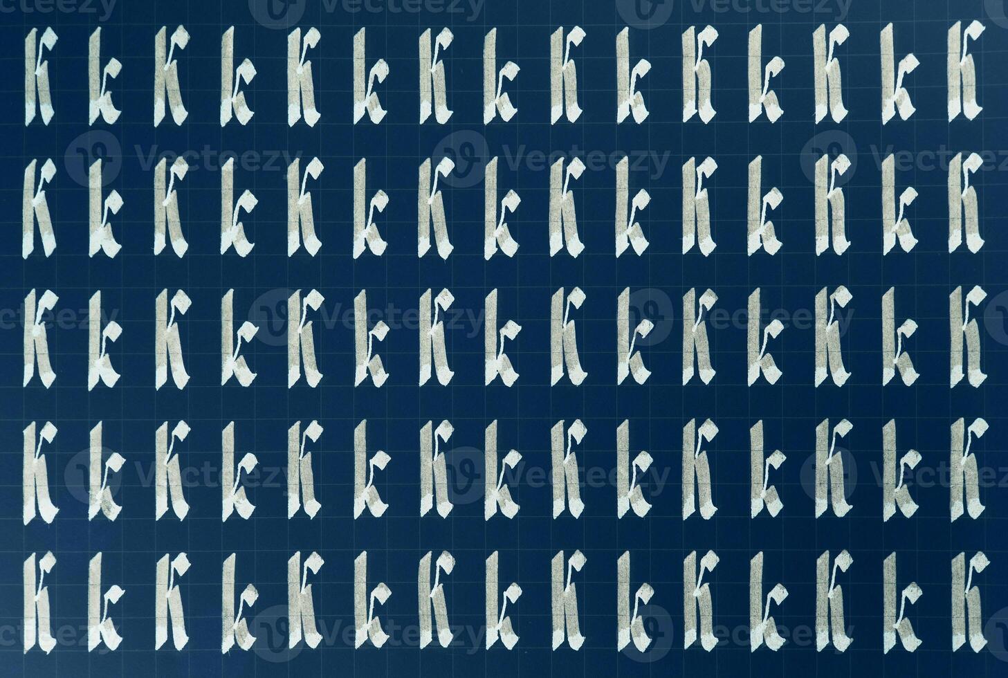 Calligraphic white on dark blue letter K learning skills paper page. Calligraphy letters k background. Lettering practice writing worksheet. Handwriting symbol filling pattern. photo