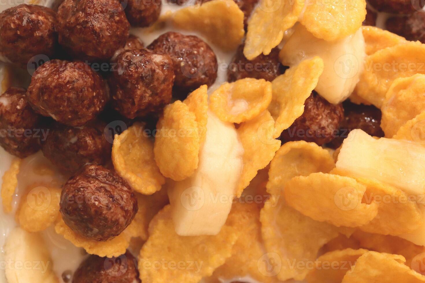 Cornflakes with chocolate balls sliced banana and milk. Filling background. Macro close-up. photo