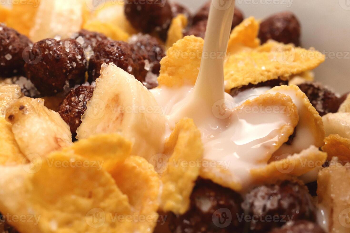 Cornflakes with chocolate balls sliced banana and stream of milk. Filling background. Macro close-up. photo