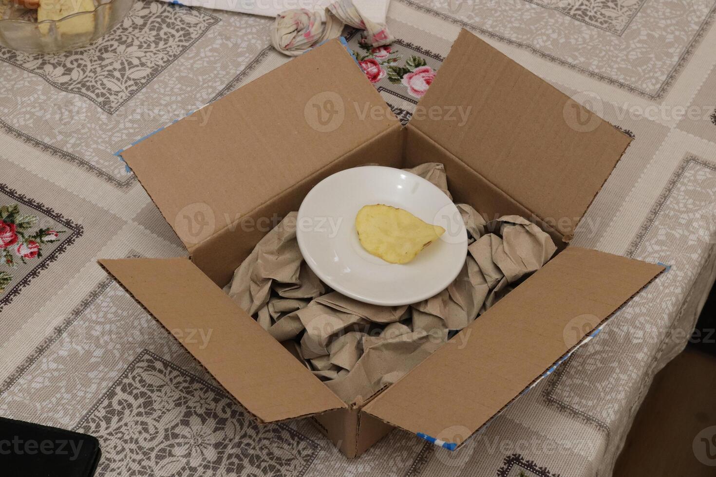 Open box with crumpled paper and plate with one crisp photo